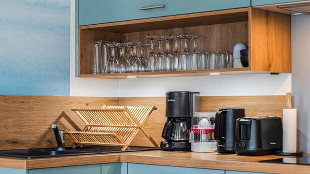 Uma cozinha com bancada de madeira, máquina de café, torradeira e suporte para copos de vinho.