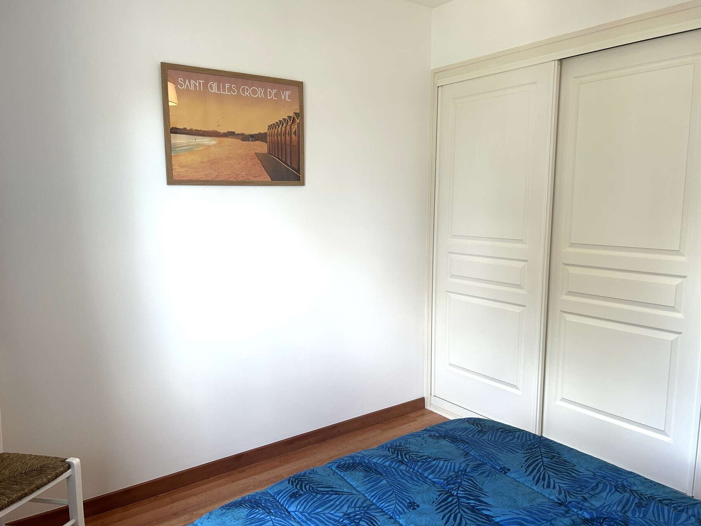 A room with a bed, a chair, a white wardrobe, and a framed picture on the wall.