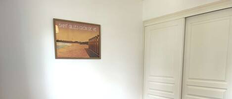 A room with a bed, a chair, a white wardrobe, and a framed picture on the wall.