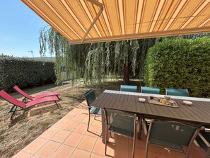 An outdoor patio with a table and chairs, a striped canopy, and a hedge in the background. - House near the sea - 4 guests (Saint-Hilaire-de-Riez)