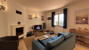 Sala de estar com lareira, televisão, sofá e janela com cortinas.