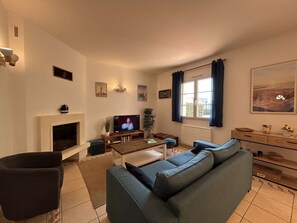 Ein Wohnzimmer mit Kamin, Fernseher, Sofa und einem fenster mit Vorhängen.