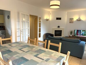 Ein Wohnzimmer mit einer Couch, einem Fernseher, einem Kamin und einem Esstisch mit Stühlen.