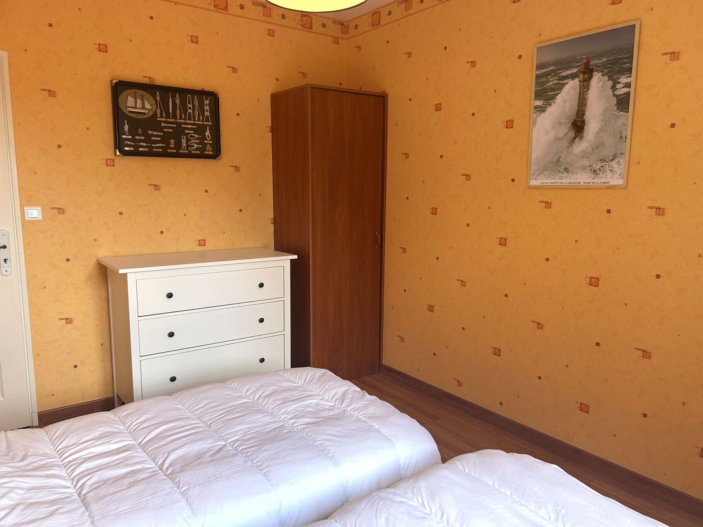 Une chambre avec deux lits, une armoire, un tableau accroché au mur et un papier peint à motifs.