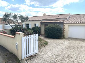 Ein Wohnhaus mit Schotterauffahrt, weißem Zaun und einem kleinen Garten mit Sträuchern und Blumen.