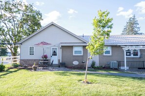 A single-story house with a front porch, a small patio with a table and chairs, and a tree in the front yard. - Quiet Amish Country Getaway | Fire Pit & Grill (Millersburg)
