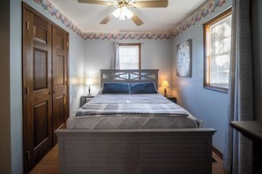 Un dormitorio con cama, dos lámparas de noche, ventilador de techo, ventana con persianas y una puerta.