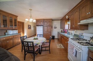 Una cocina con armarios de madera, una mesa de comedor con sillas, un refrigerador, una estufa y un microondas.