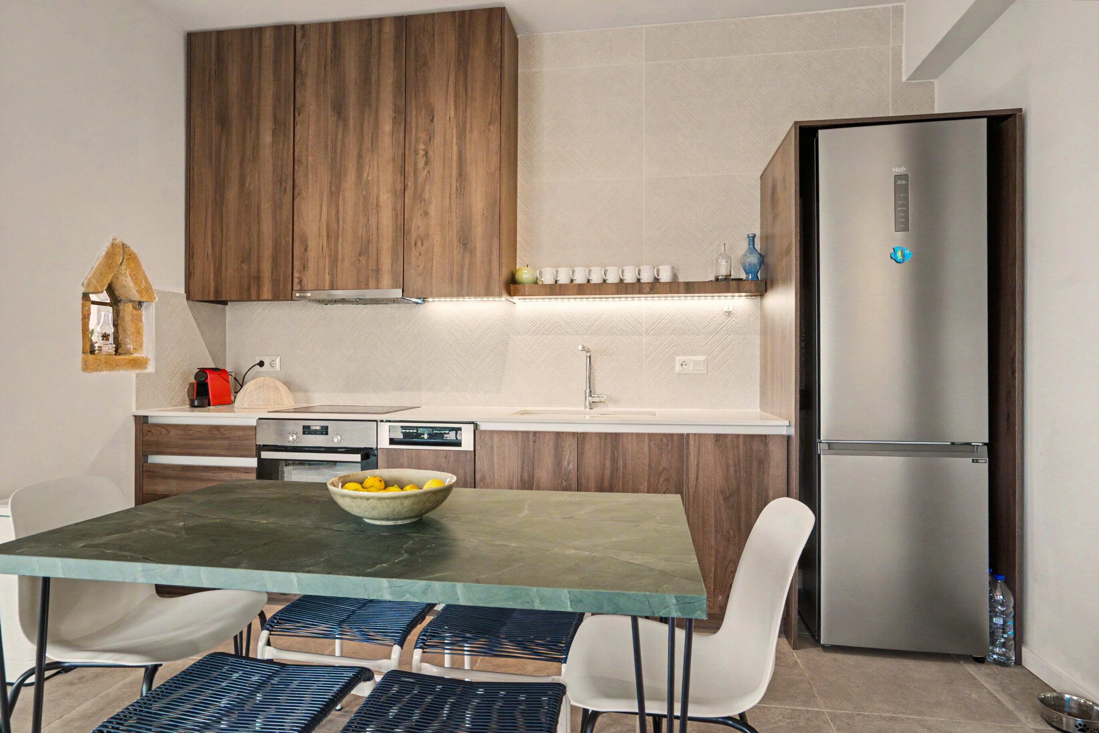 Une cuisine moderne avec des meubles en bois, un réfrigérateur en acier inoxydable et une table à manger avec des chaises.