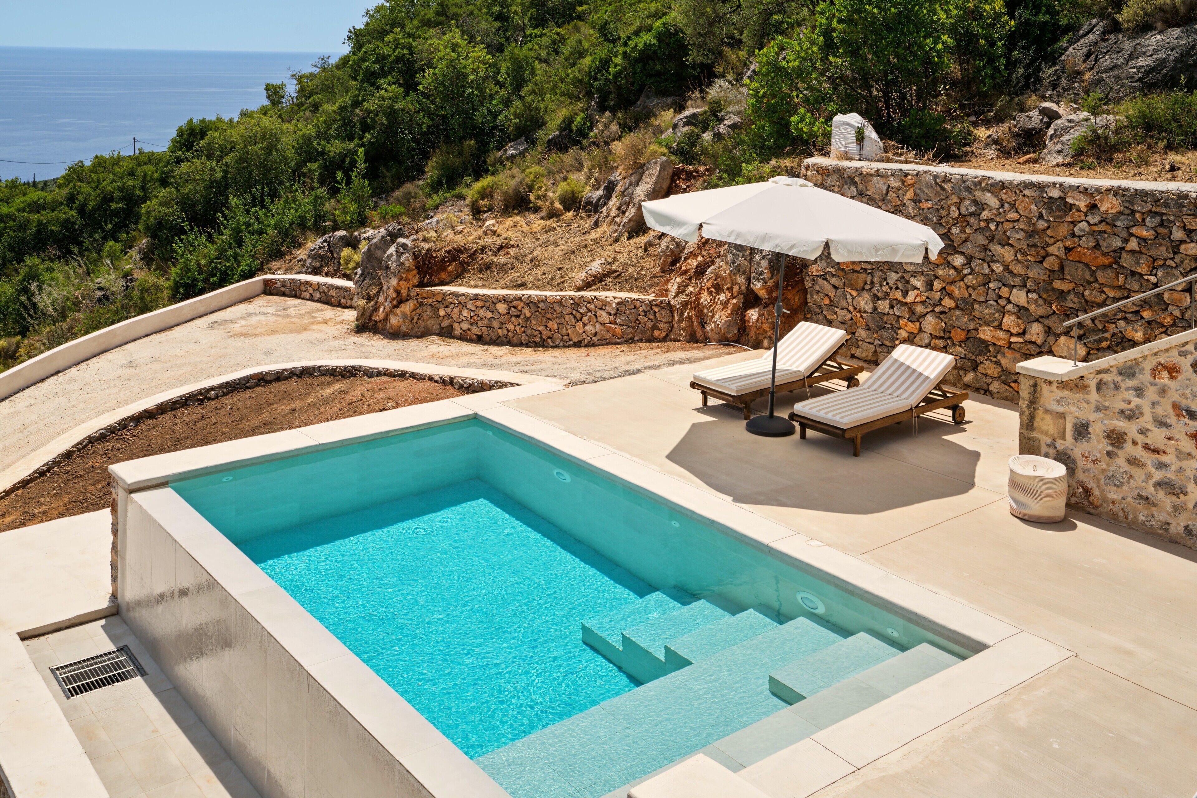 Una piscina con muro de piedra y vista al mar.