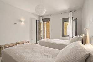 Een moderne slaapkamer met twee bedden, een bankje en een groot raam met gordijnen.