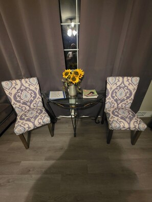 Un comedor con dos sillas estampadas, una mesa de cristal, un jarrón con girasoles y un libro.