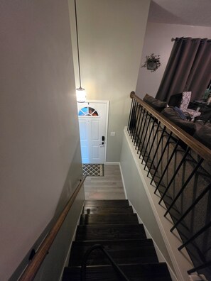 A staircase with a wooden handrail and a black metal railing, leading to a door with a decorative glass panel.