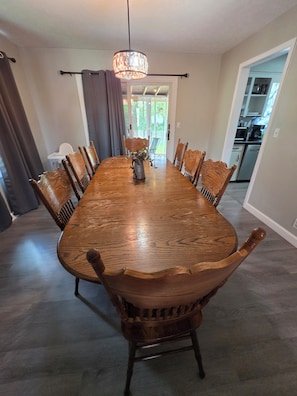 Comedor con una gran mesa de madera, sillas, candelabro y vista al exterior.