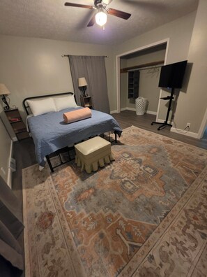 A bedroom with a bed, bedside tables, a ceiling fan, a TV stand, and a patterned rug.