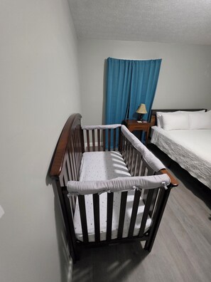 A room with a crib, a bed, a nightstand, and a blue curtain.