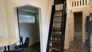 A loft-style room with a mezzanine, a staircase, a dining area with chairs, and a kitchen area. - Sunrise Cottage at River Rocks Landing (Gadsden)