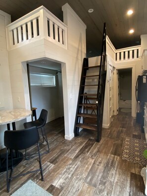 Ein Loft-Zimmer mit Schlafgalerie, einer Wendeltreppe, einem Essbereich mit Stühlen und einer Küchenzeile.