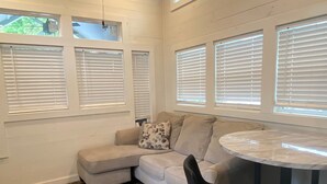 A room with a sectional sofa, a round table, and multiple windows with blinds. - Sunrise Cottage at River Rocks Landing (Gadsden)