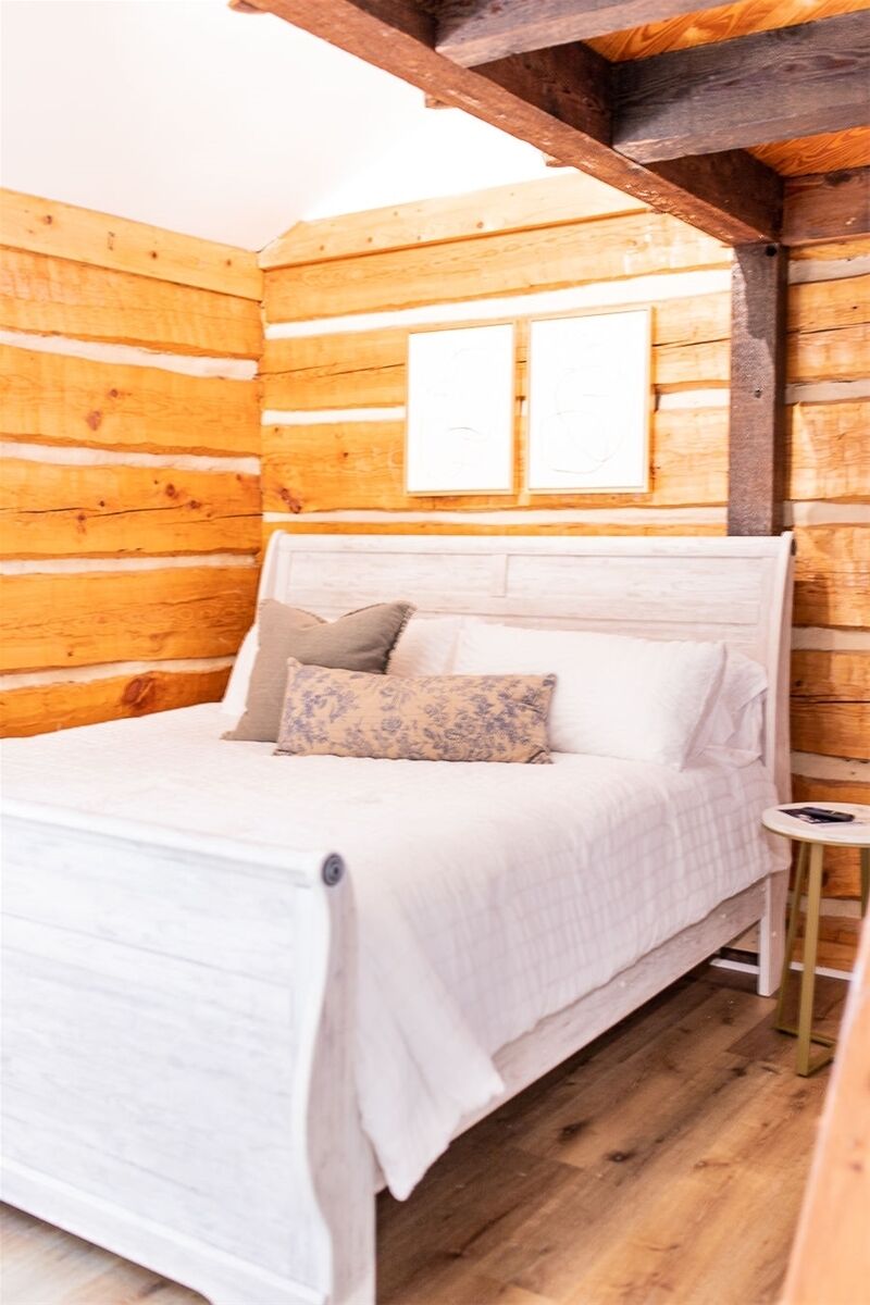 Ein Zimmer in einer Holz-Blockhütte mit einem Bett, einem kleinen Nachttisch und einem Fenster.