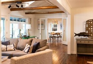 Ein geräumiges Wohnzimmer mit Holzbalkendecke, einem Essbereich und einer im Hintergrund sichtbaren Küche.