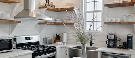A modern kitchen with white cabinetry, stainless steel appliances, and wooden shelves.