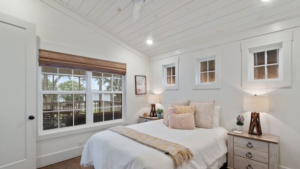 Quarto com cama grande, duas mesas de cabeceira, janela com persianas e teto de madeira.
