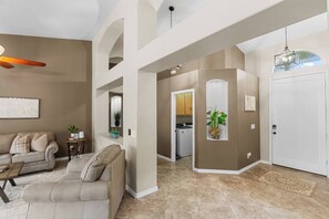 A spacious living room with a sofa, a coffee table, and a dining area. There is a kitchen visible in the background.