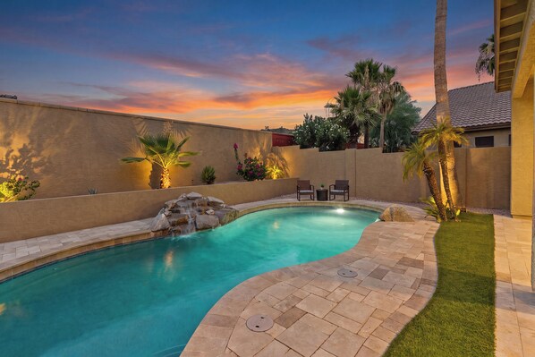 A swimming pool with a curved edge, surrounded by a low wall and a grassy area.
