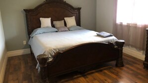 Quarto com cama de madeira, janela com cortinas e chão de madeira.