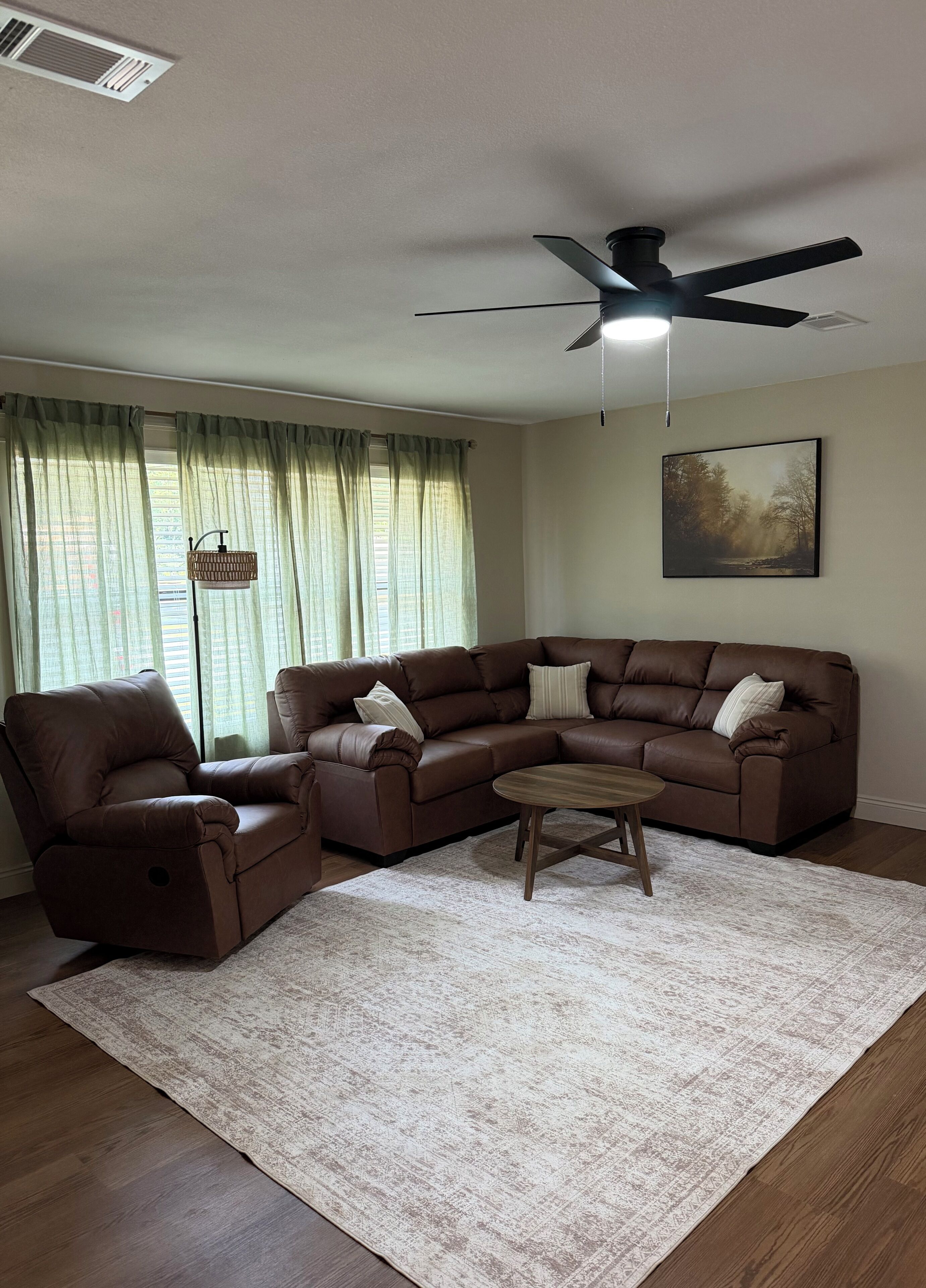 A living room with a sectional sofa, a recliner, a coffee table, a ceiling fan, and a painting on the wall.