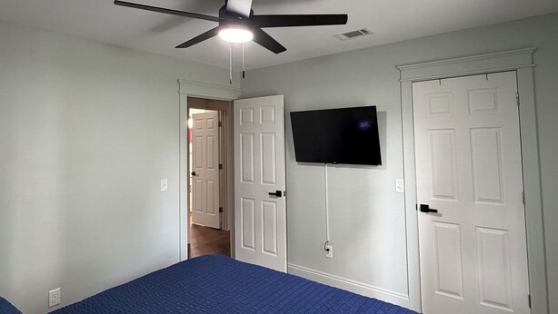 A bedroom with a bed, a ceiling fan, a television mounted on the wall, and a door. - Kimberly House (Mena)