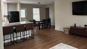 A modern kitchen with a black refrigerator, a dining area with wooden chairs, a ceiling fan, and a flat-screen TV mounted on the wall. - Kimberly House (Mena)