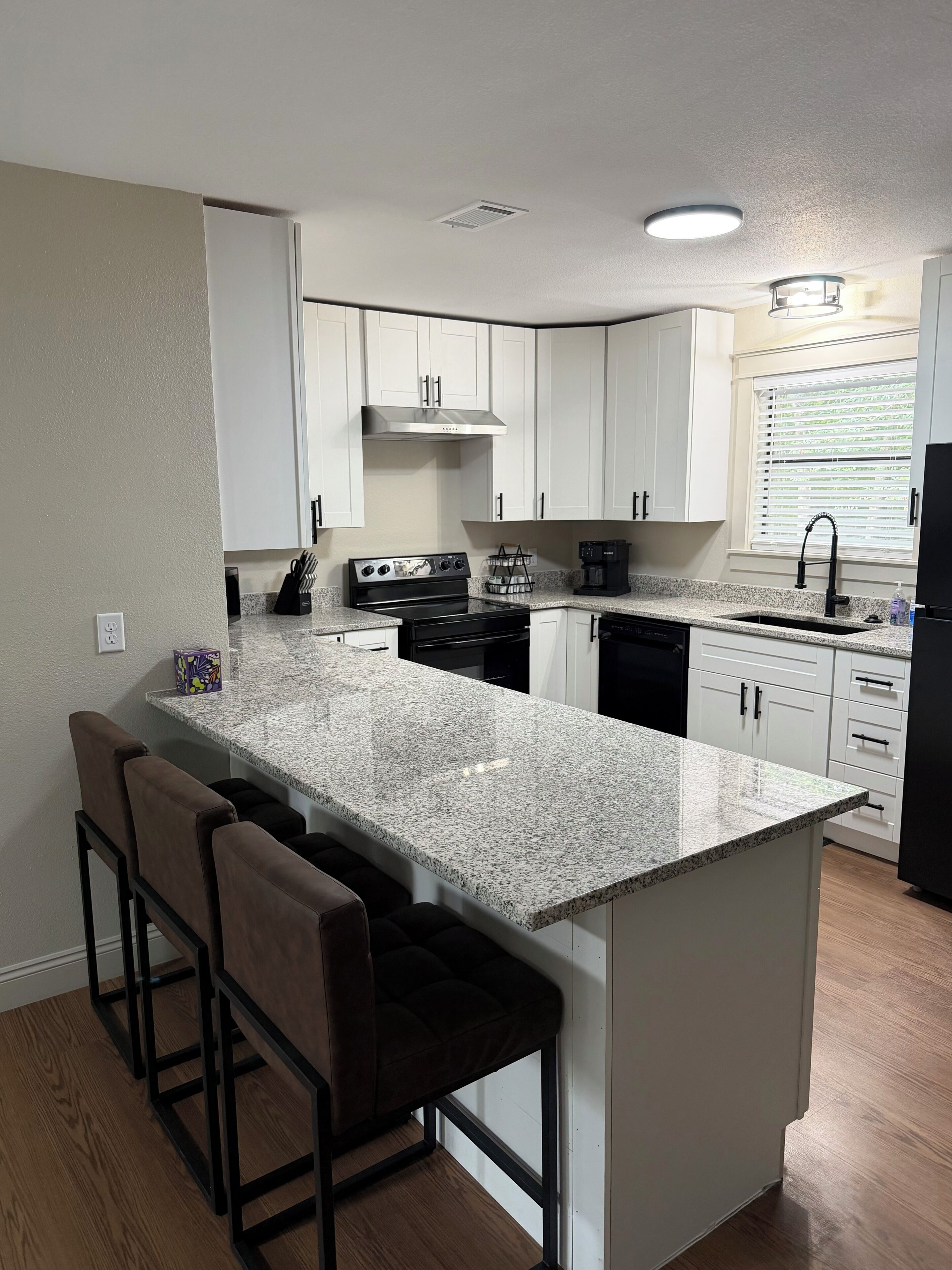 A modern kitchen with white cabinets, a granite countertop, a black stove, and a built-in island with bar stools.