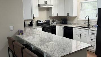 A modern kitchen with white cabinets, a granite countertop, a black stove, and a built-in island with bar stools.