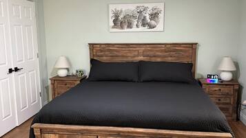 A bedroom with a bed, wooden headboard, bedside tables, a ceiling fan, and a wall-mounted artwork.