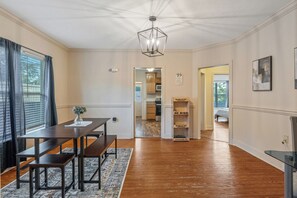Ein Essbereich mit Holztisch und Bänken, einer Chandelüster und Blick in die Küche.