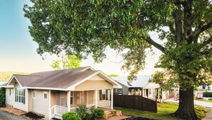Una casa de una sola planta con porche, patio cercado y un gran árbol.