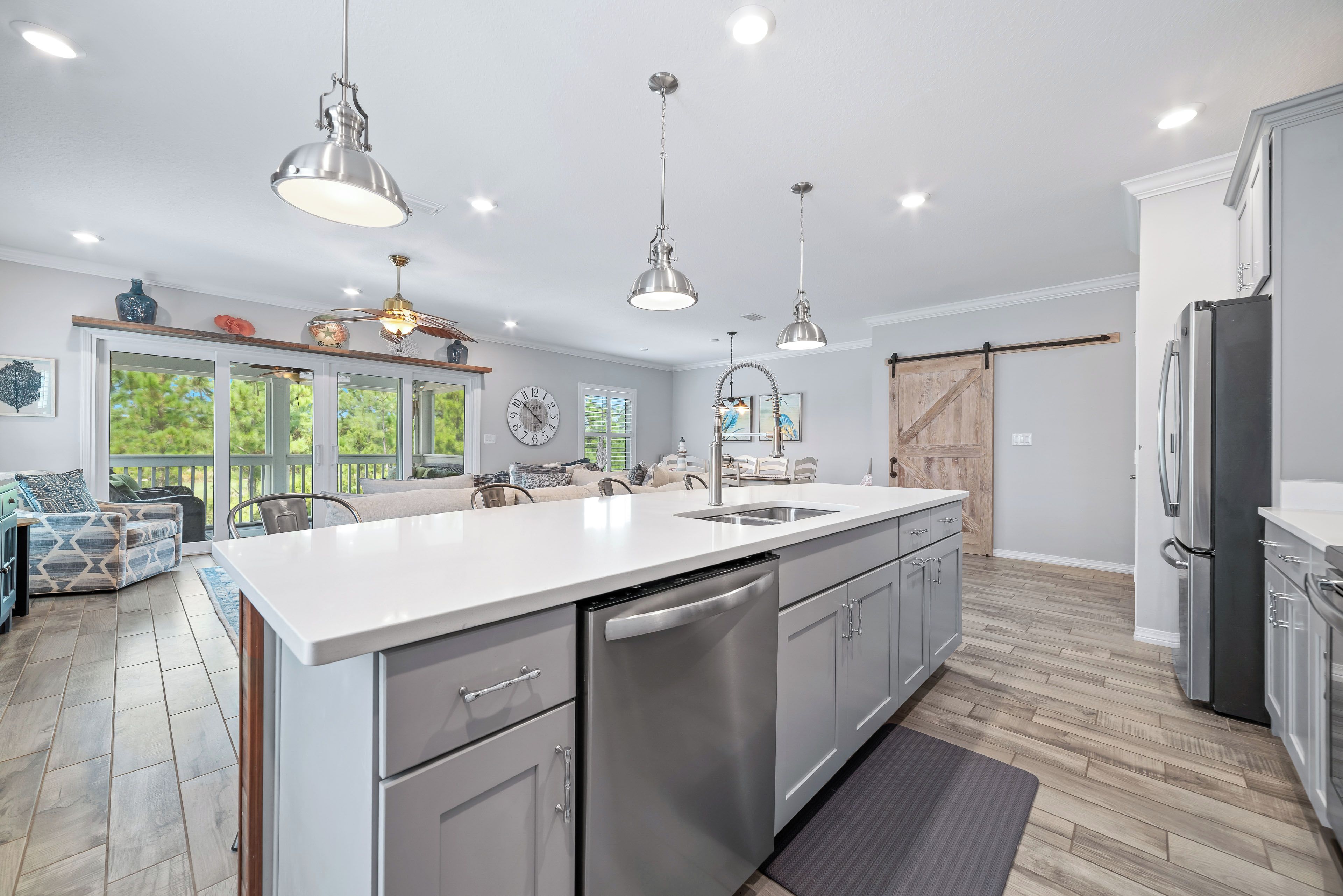 A modern kitchen with a central island, stainless steel appliances, pendant lighting, and a view to the outdoors.