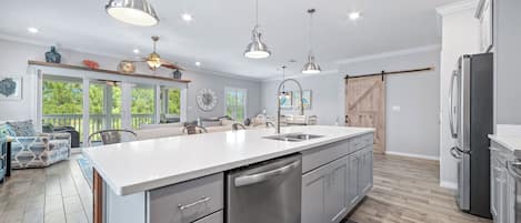 A modern kitchen with a central island, stainless steel appliances, pendant lighting, and a view to the outdoors.