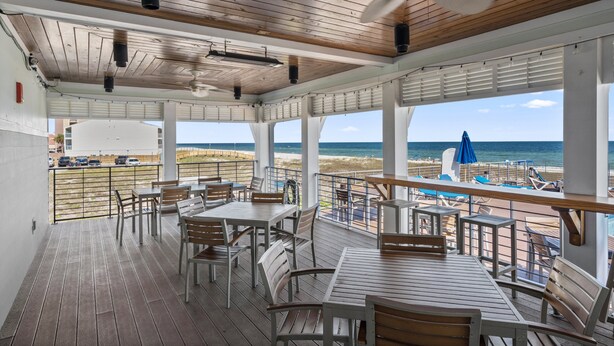 Una terrazza coperta all'aperto con tavoli e sedie di legno, con vista su una spiaggia e l'oceano.