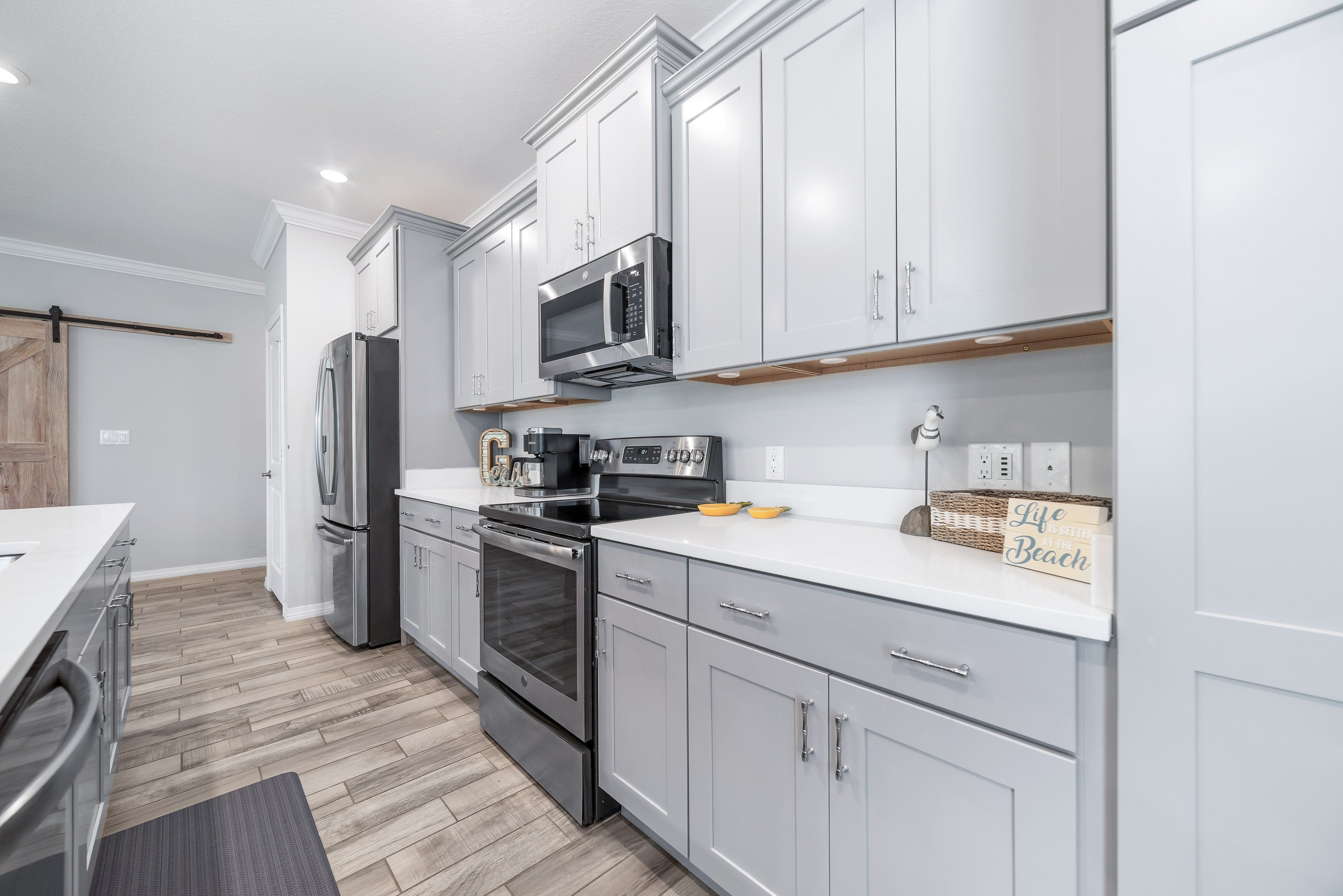 A modern kitchen with stainless steel appliances, white cabinetry, and a wooden floor.