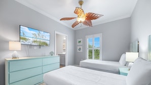 Una camera da letto con due letti, televisione, ventilatore a soffitto e vista sull'esterno da una finestra.