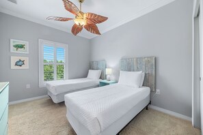 A bedroom with two beds, a ceiling fan, a window with blinds, and artwork on the wall. - Coral Barracks at Lost Key Golf & Beach Club | Resort Amenities | My Beach Getaways (Pensacola)