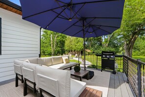 A covered outdoor deck with a sofa, a grill, and a large umbrella. - Luxury Designer Retreat on 1.3 Acres with Game Lounge (Fort Wayne)
