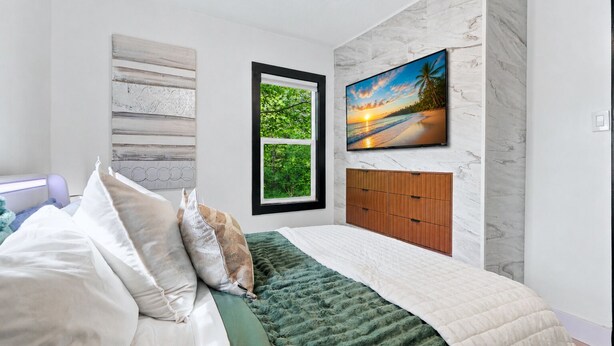 Quarto com uma cama, janela, televisão fixada na parede e um armário de madeira.