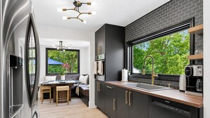 Uma cozinha moderna com um revestimento de tijolos pretos, eletrodomésticos de aço inoxidável e uma janela grande com vista para o verde.