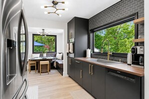 A modern kitchen with a black brick backsplash, stainless steel appliances, and a large window offering a view of greenery.