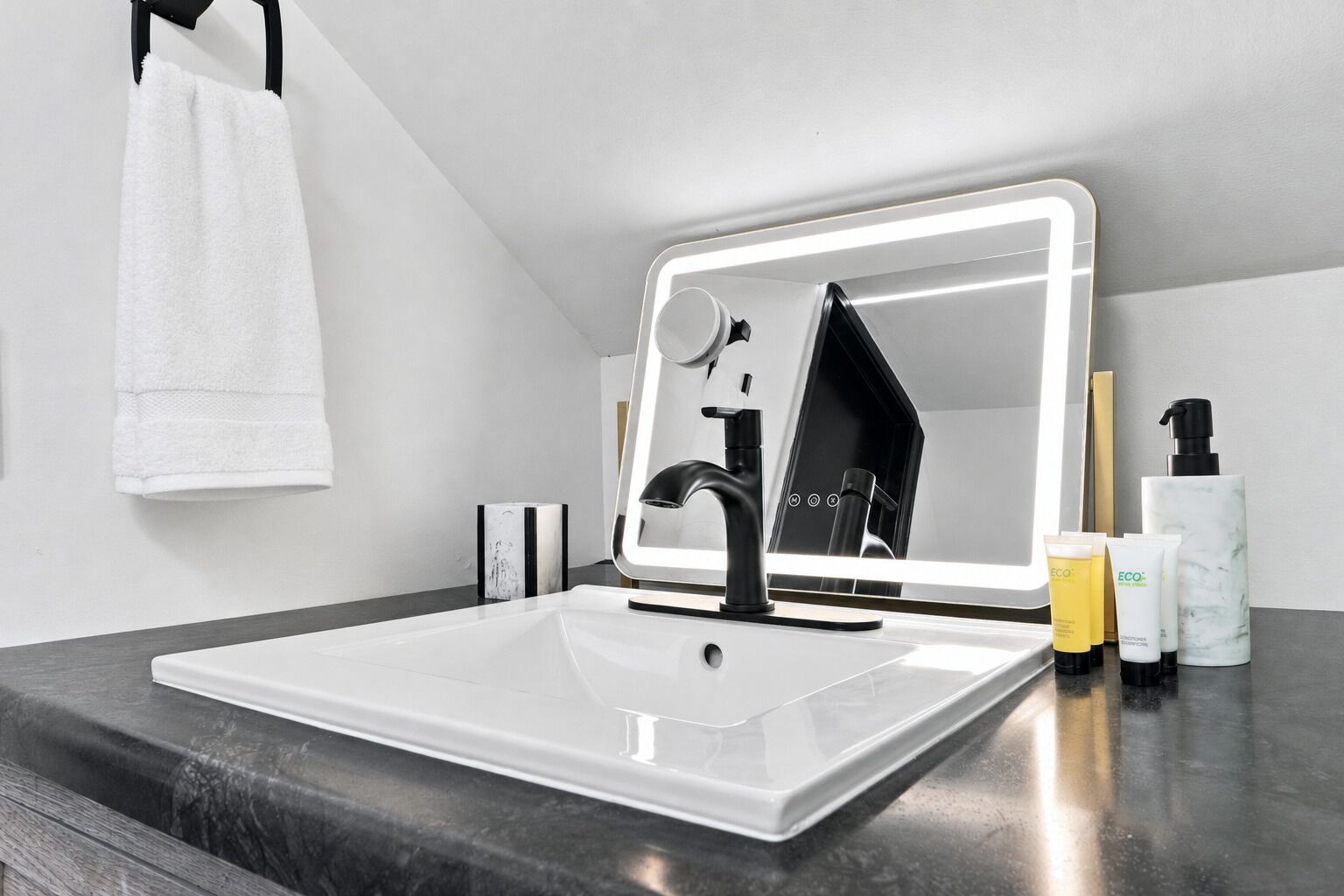 A modern bathroom with a large mirror, a black faucet, and a white sink.