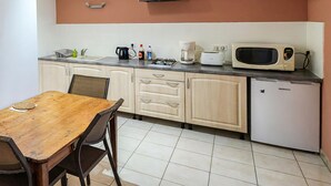 Eine kleine Küche mit Holztisch, Schränken, einer Mikrowelle, einer Kaffeemaschine und einem Kühlschrank.